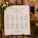 Wedding seating chart on an easel at the entrance of an elegant Orlando wedding reception with floral décor and guest tables.