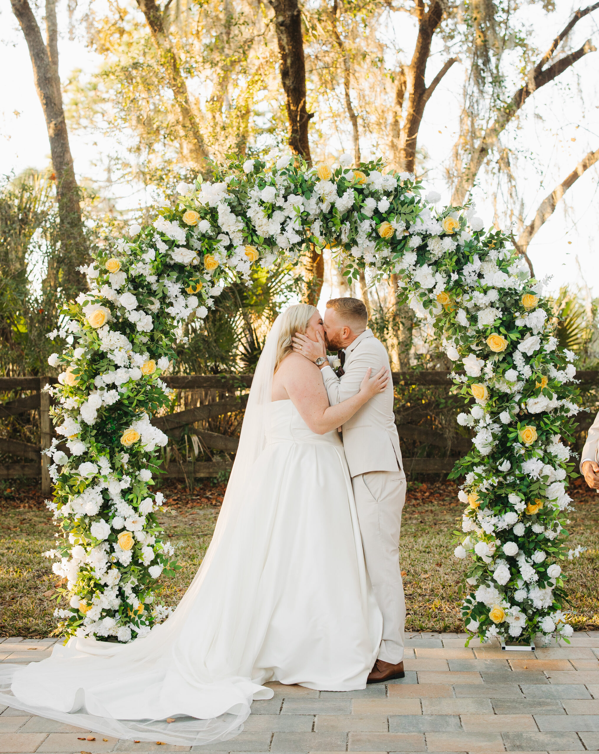 Newlyweds Travis and Sydney kissing beneath their floral wedding arch at The Farmhouse on 44.