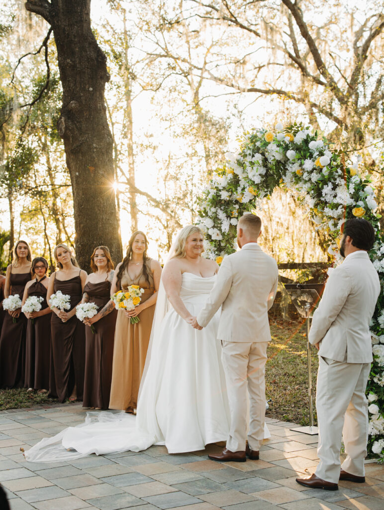 Travis and Sydney standing together at their floral arch during their outdoor ceremony at The Farmhouse on 44.