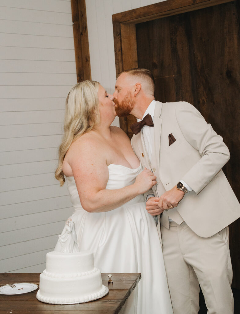 Travis and Sydney kissing beside their wedding cake during their reception.
